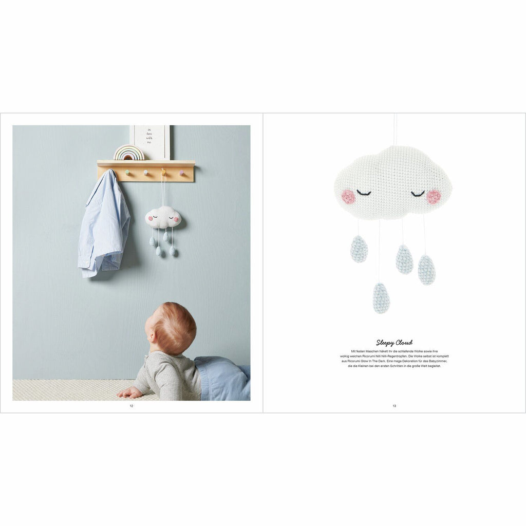 Ein Baby schaut sich eine gehäkelte Regenwolke an, die Regenwolke hat schlafende Augen aufgestickt und es hängen 4 Regentropfen in Hellblau herunter. 